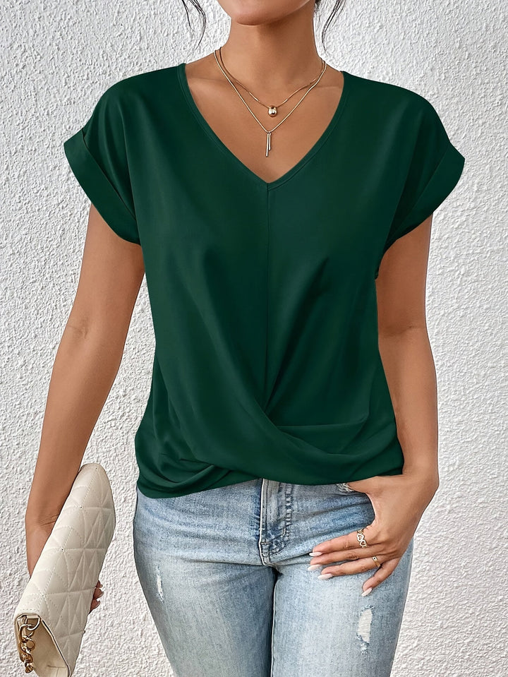 Forest green V-neck T-shirt with rolled sleeves, styled with light jeans and a white quilted clutch, against a textured white wall.