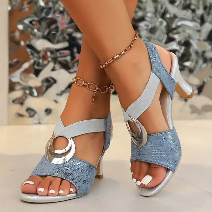 Blue supportive heel sandals with metallic accents, worn on feet, indoor setting with blurred background.