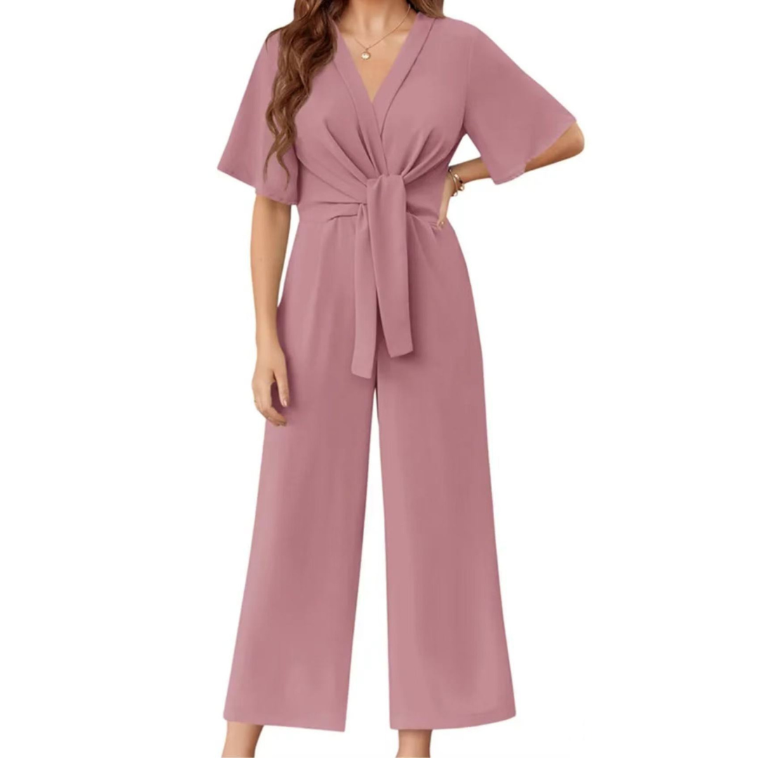 Pink elegant jumpsuit with short sleeves and a tie waist on a woman, studio background.