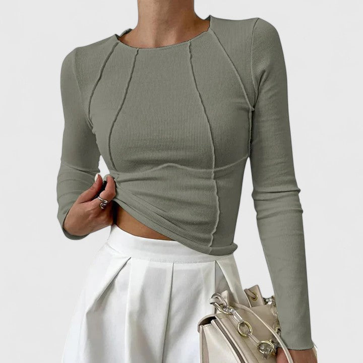 Olive green long-sleeve top with curved seam details, matched with a white skirt and beige handbag, on a plain white background.