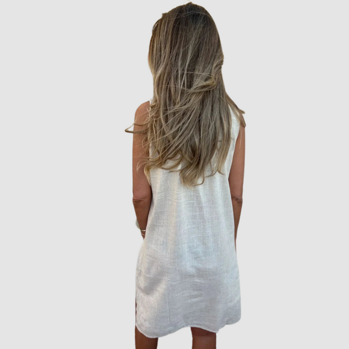 Back view of a woman in a light sleeveless dress, showcasing long hair in a simple studio background.