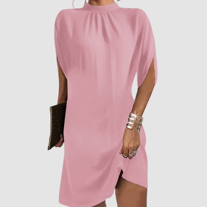 Pink knee-length dress with a flowing fit and high neck, styled with gold bangles and clutch against a gray background.
