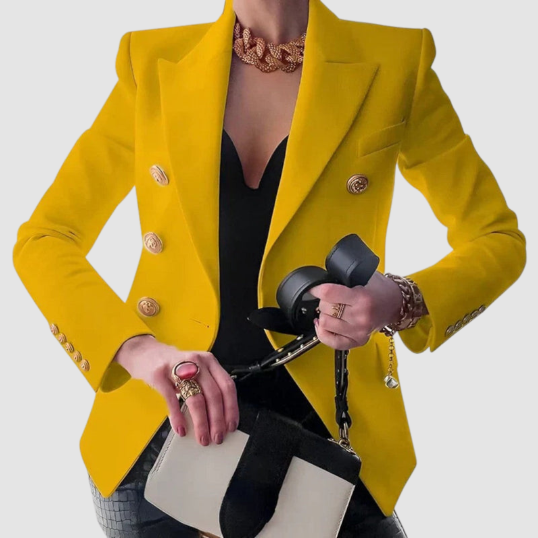 Bright yellow blazer with gold buttons, paired with a black top. Gold jewelry and a beige handbag complement the look in a studio setting.