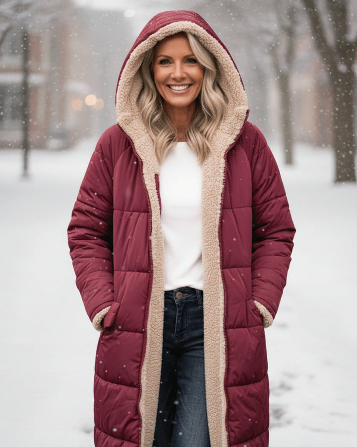 Woman in red hooded coat, smiling among snowflakes in a snowy urban scene.