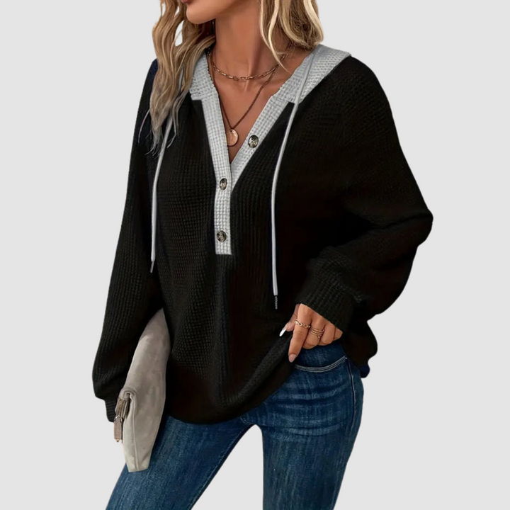 Black knitted long sleeve hoodie with contrasting trim and drawstrings, worn with blue jeans against a gray studio backdrop.
