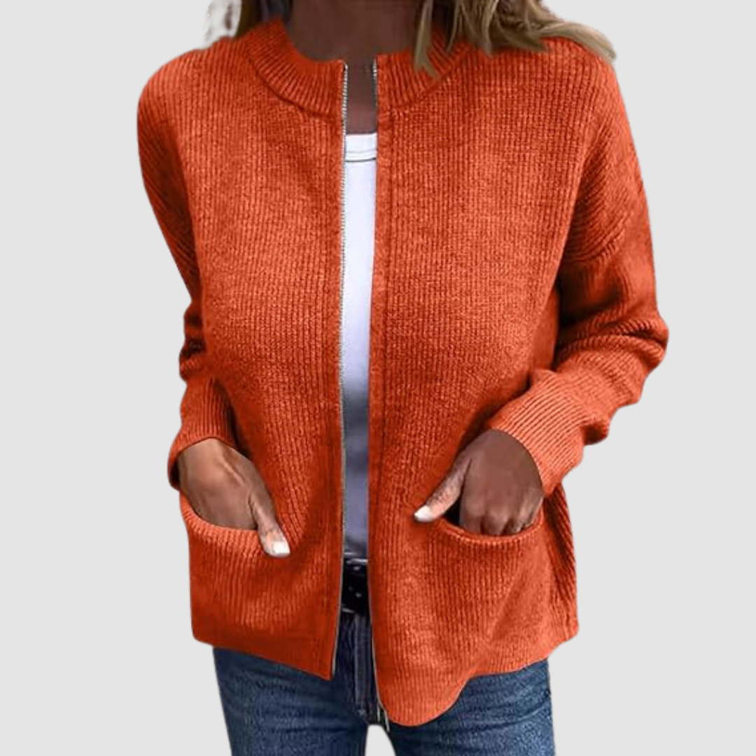 Orange cozy cardigan worn over a white t-shirt with hands in pockets. Neutral background.