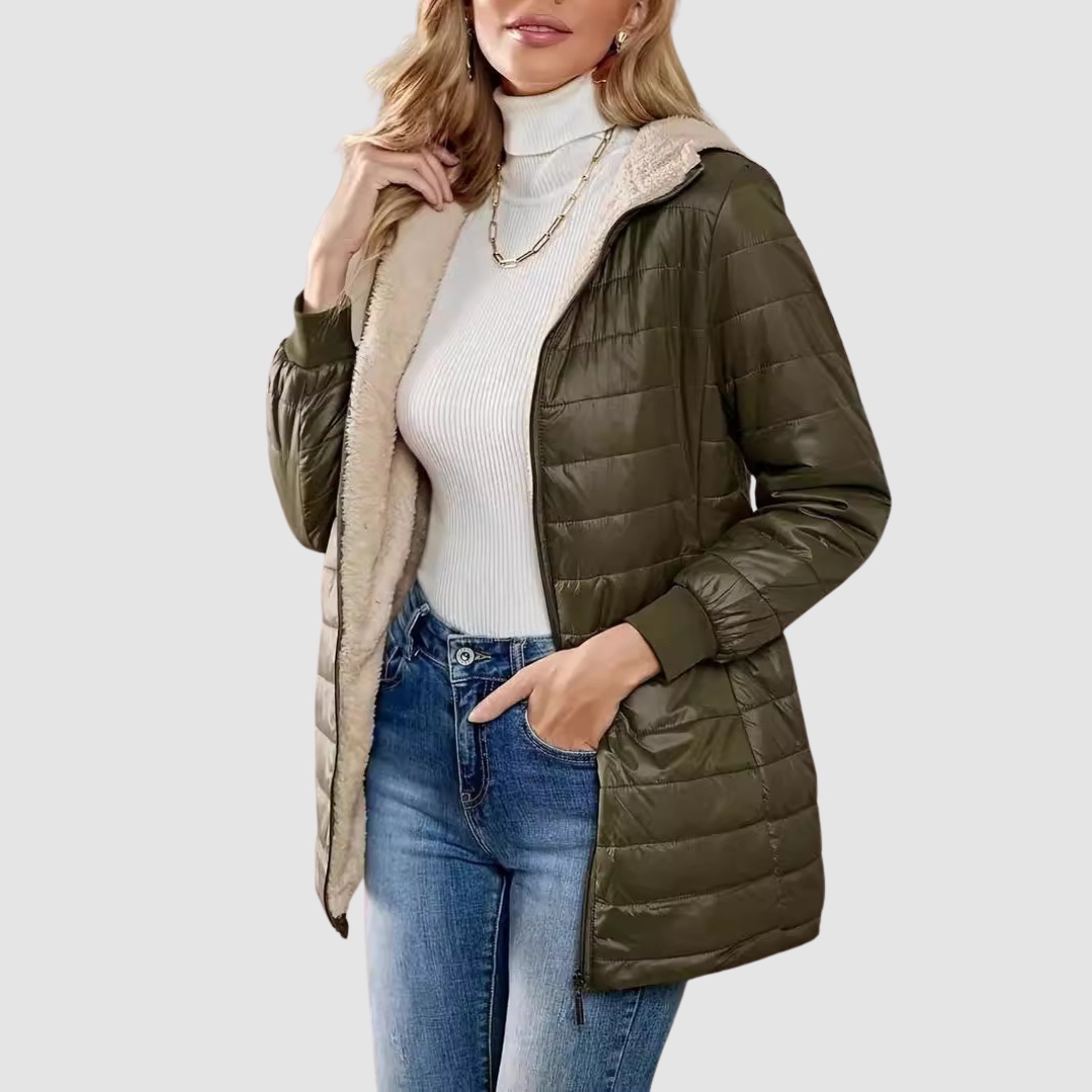 Woman wearing an olive green winter coat with a white turtleneck, jeans, and a chain necklace, studio setting.