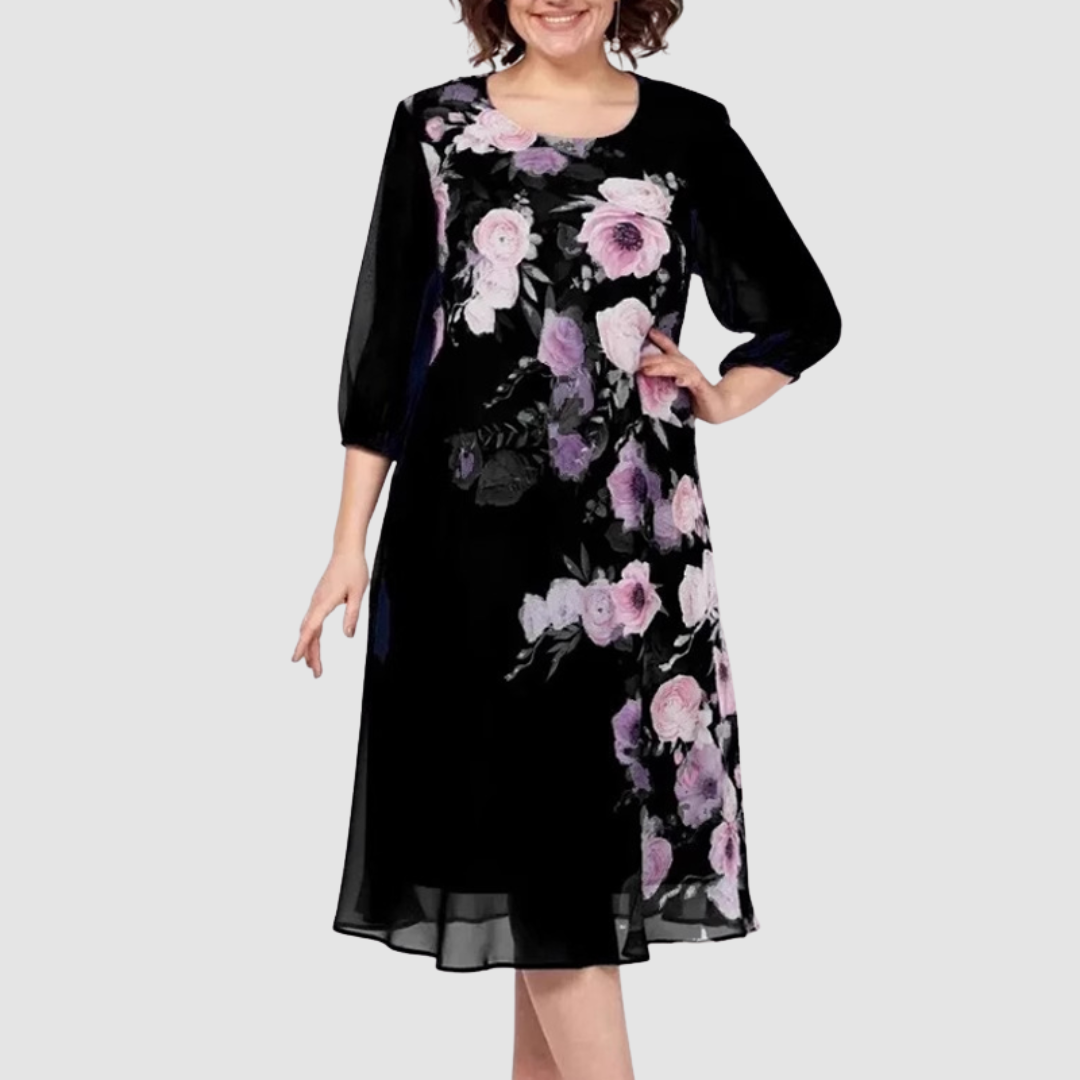 Model wearing a black floral dress with vibrant pink and purple flowers, in a studio with a light background.