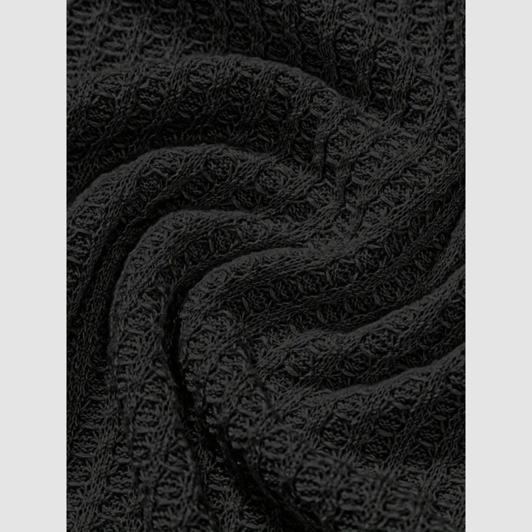 Close-up of black fabric with a woven, textured pattern in soft folds. Plain light gray background.