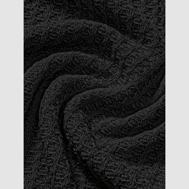 Close-up of black fabric with a woven, textured pattern in soft folds. Plain light gray background.