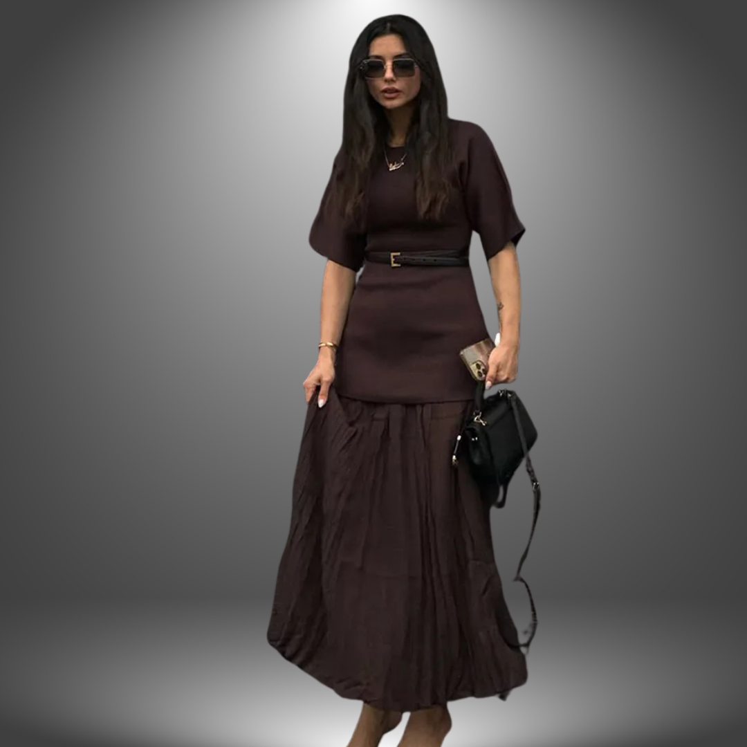 Woman wearing elegant dark brown dress, accessorized with sunglasses and black handbag, standing in a gradient studio setting.