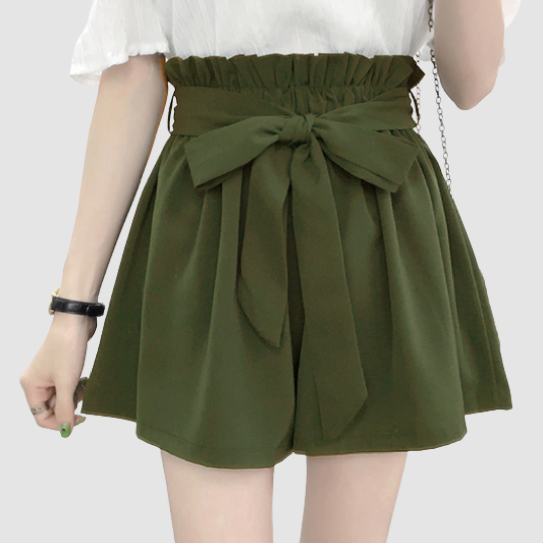Green paperbag waist shorts with a bow, paired with a white top in a studio background.