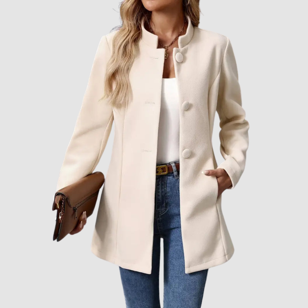 Light beige jacket, large buttons, worn over white top and jeans, holding clutch, plain background.