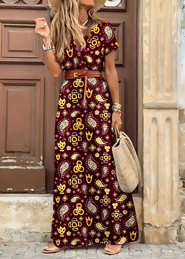 Woman wearing patterned dress with brown belt, holding straw bag, standing by wooden door outdoors.