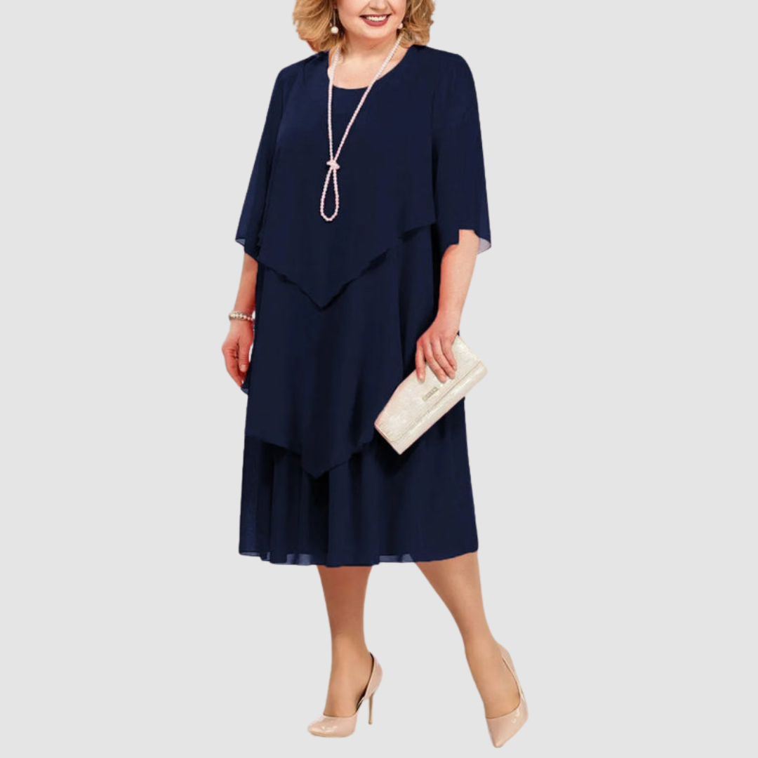 Navy chiffon midi dress with layered design, accessorized with pearl necklace and beige clutch, on white background.