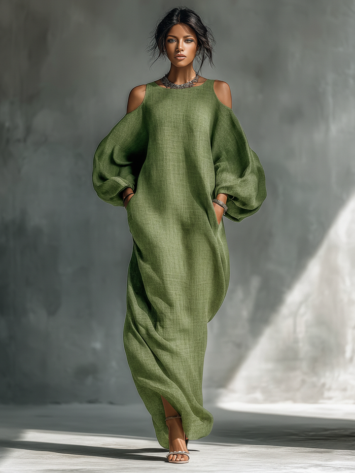 Model in flowing green maxi dress with cutout shoulders and long sleeves, standing in a studio setting.