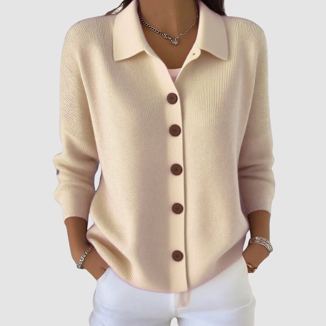 Beige button-up knit cardigan with brown buttons, worn with white pants in a studio setting.