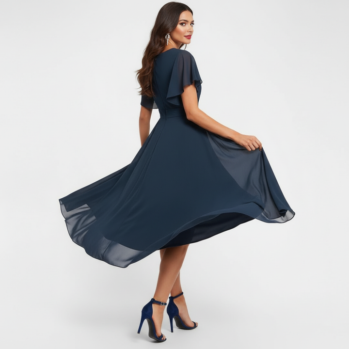 Angled view of woman in navy flowing V-neck maxi dress with flared hem and short sleeves, in a studio setting.