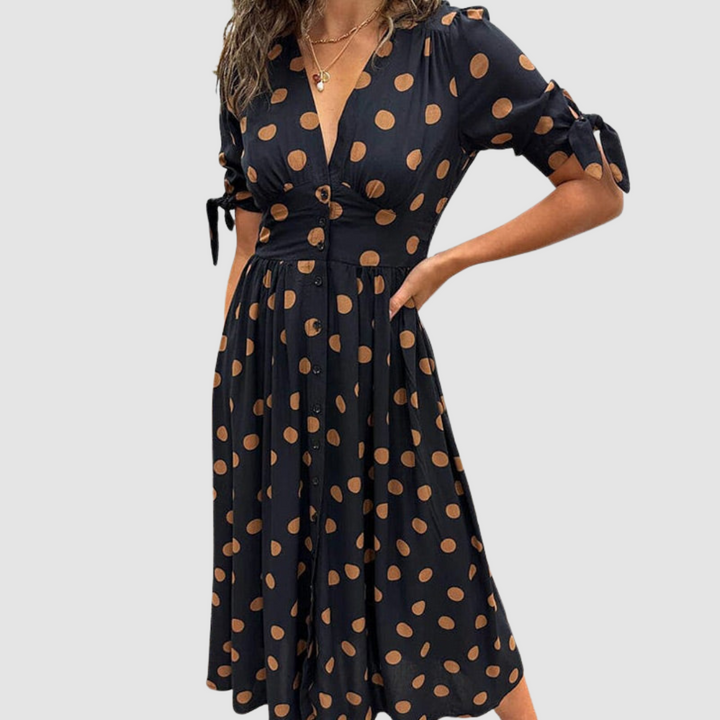 Black dress with orange polka dots, V-neck, tied sleeves, knee-length, studio setting.