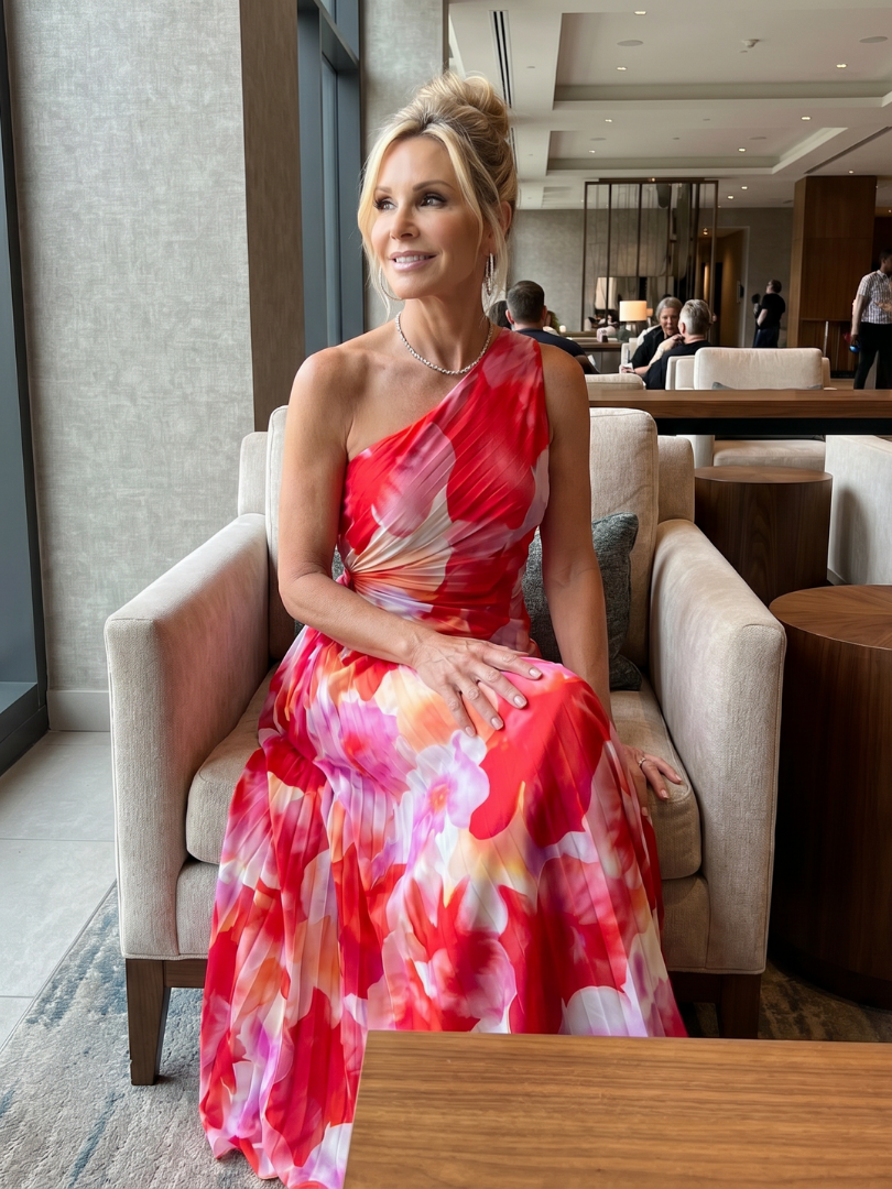 Model seated in elegant indoor lounge wearing red floral one-shoulder midi dress.