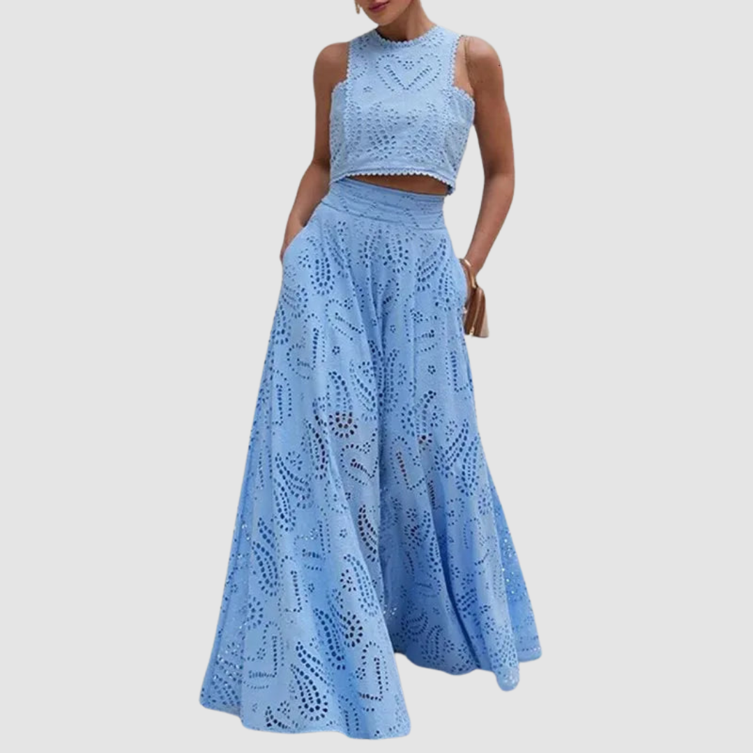 Model in a blue two-piece outfit with cutout details, wide pants, standing with hands in pockets on white background.