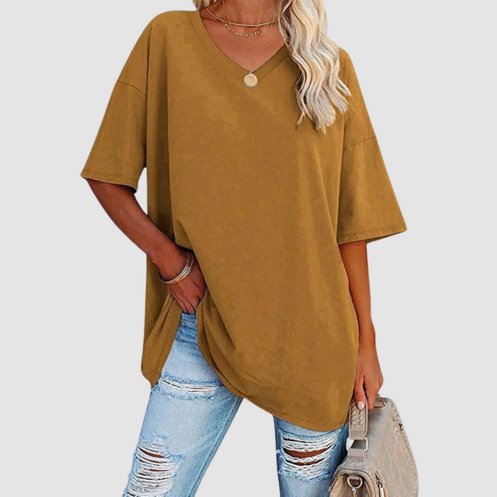 Woman in a mustard V-neck T-shirt with distressed jeans, carrying a beige bag, studio setting.