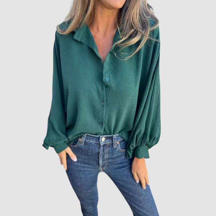 Model wearing a green oversized blouse with buttons, blue jeans, hands in pockets, gray background.