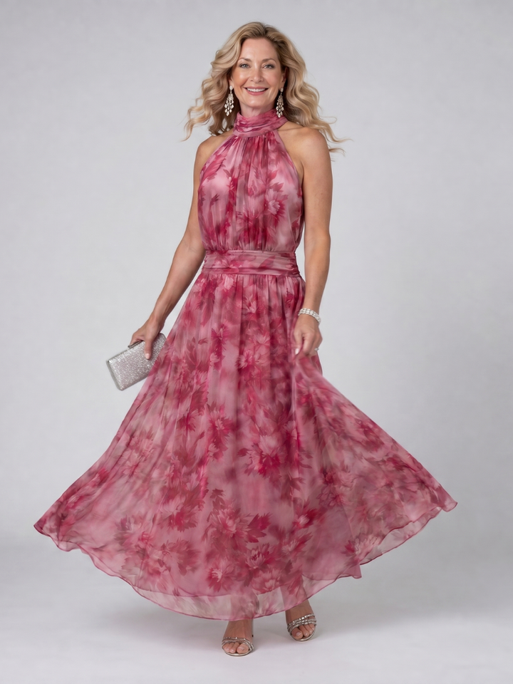 Woman twirling in pink floral halter neck midi dress, holding silver clutch, in studio setting.