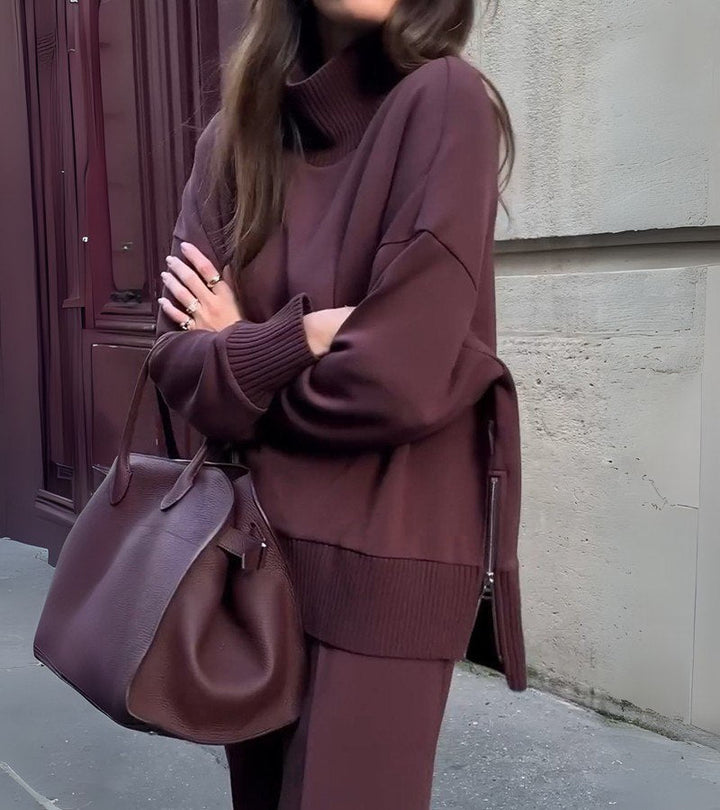 Woman in a burgundy two-piece set, arms crossed, standing against a metal and concrete wall.