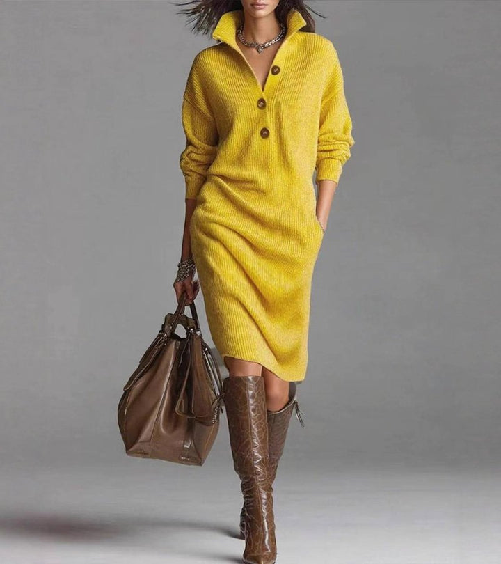 Model in a chic yellow knit dress with buttons, holding a brown bag. Studio setting with a gray background.