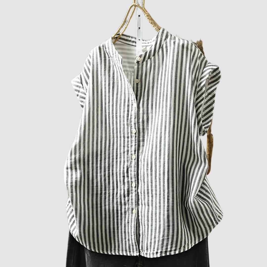 Black and white vertical striped vintage shirt with short sleeves hanging on a rustic branch against a gray background.