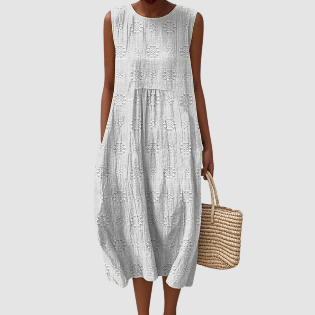 White sleeveless summer dress with floral patterns, model holding a woven basket, white background.