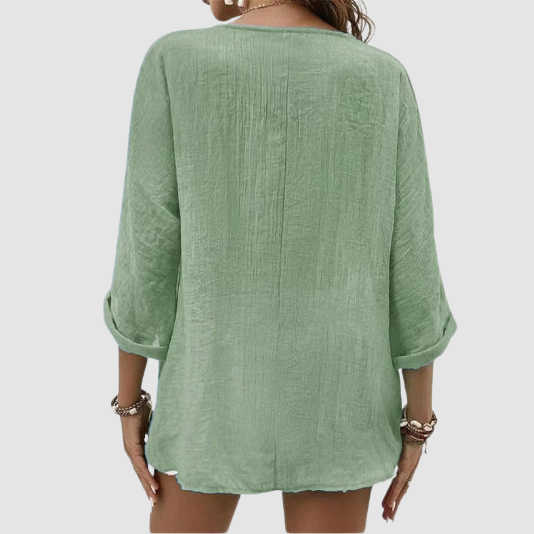 Back view of woman wearing a green three-quarter sleeve blouse, accessorized with bracelets, against a plain background.