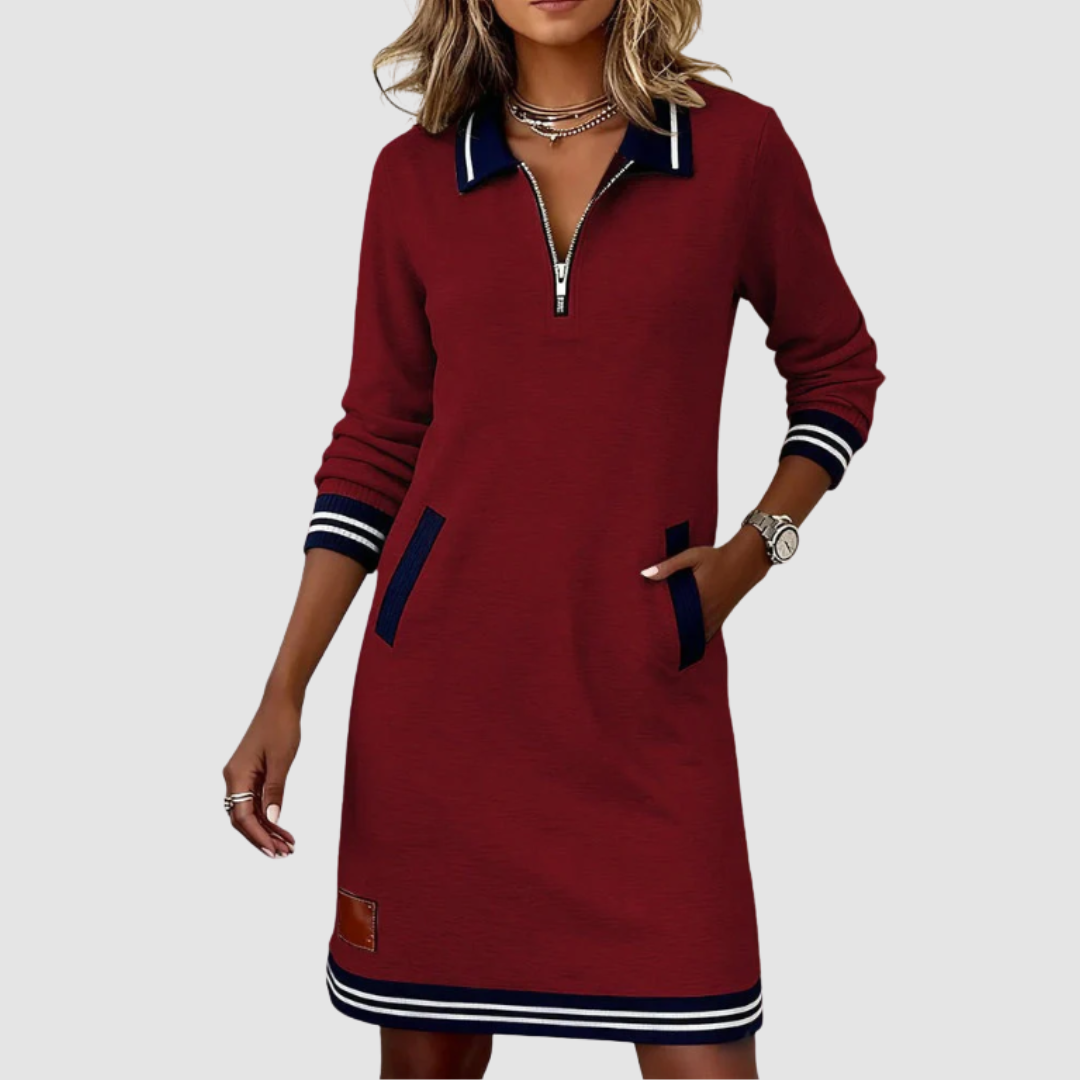 Trendy burgundy zip-neck dress with navy accents and pockets, worn by a fashionably accessorized woman in a studio.