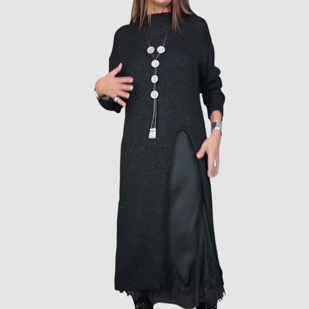 Long black dress with textured material, highlighted by a layered fabric slit and necklace, studio background.