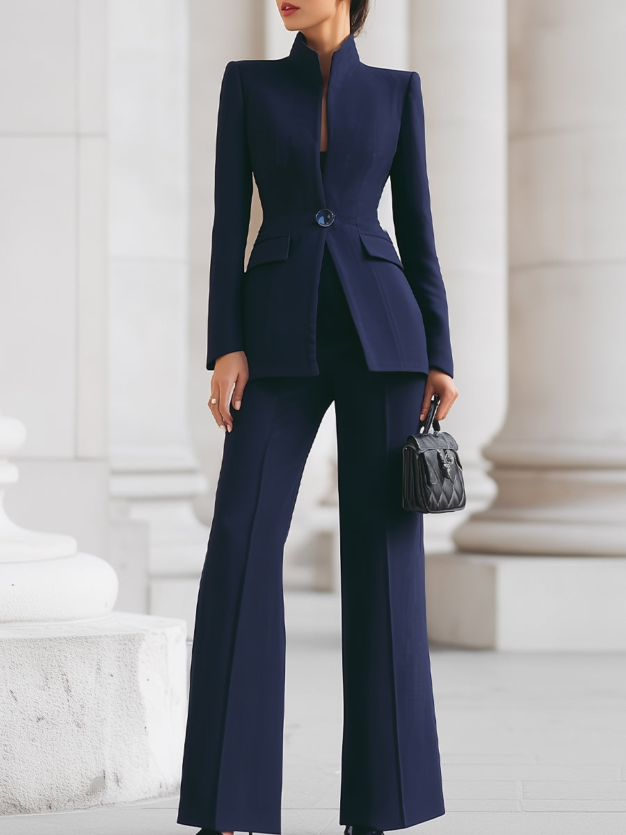 Dark blue tailored two-piece set with fitted jacket and flared pants, shown in an elegant architectural setting.