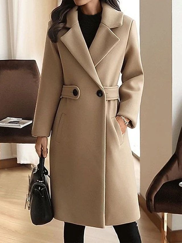 Sophisticated beige coat with broad lapels and button embellishments, presented in an indoor environment. Model holds a black handbag.