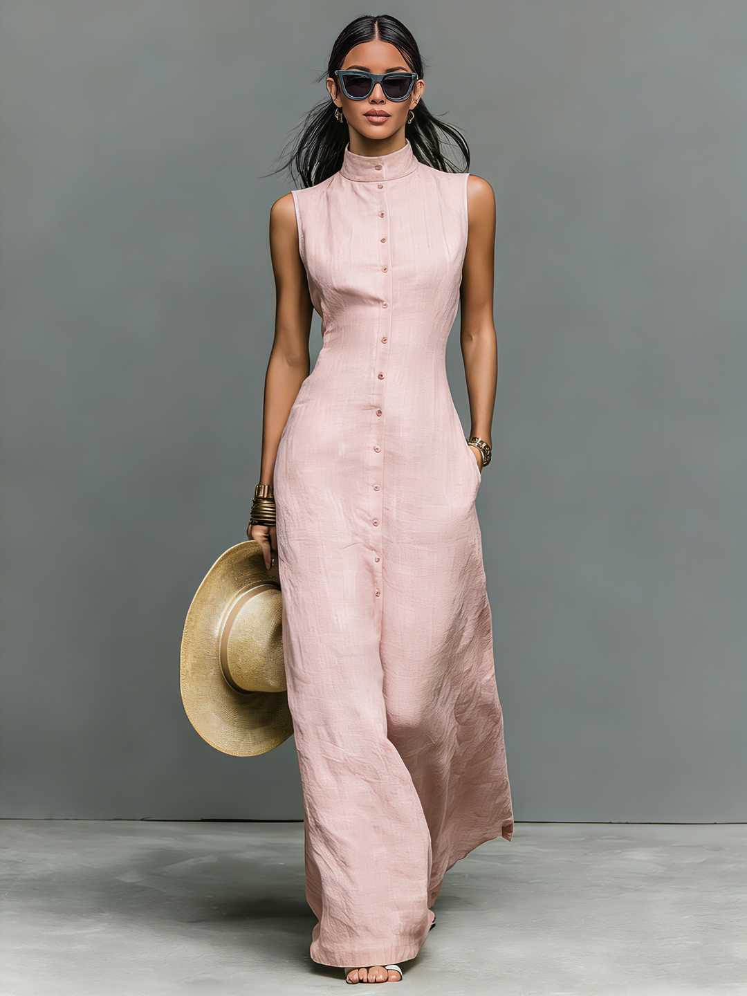 Model in a pink sleeveless maxi dress holding a wide-brim hat in a studio setting.