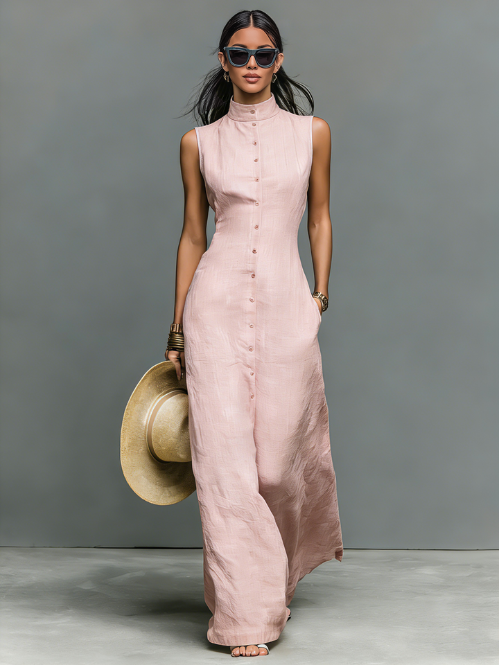 Model in a pink sleeveless maxi dress holding a wide-brim hat in a studio setting.