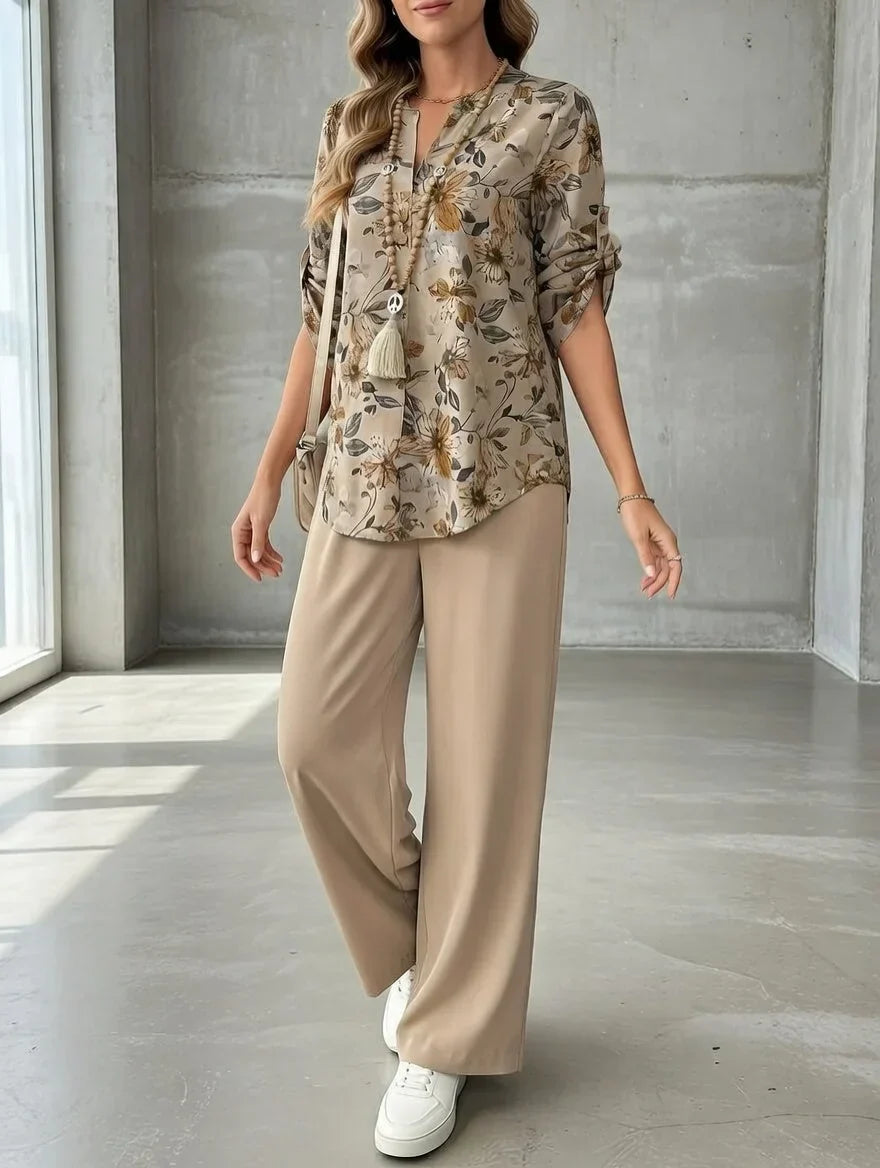 Person modeling a floral blouse and beige wide-leg pants in a sunlit concrete-walled studio.