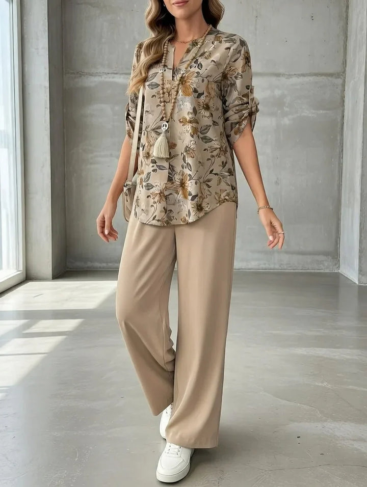 Person modeling a floral blouse and beige wide-leg pants in a sunlit concrete-walled studio.