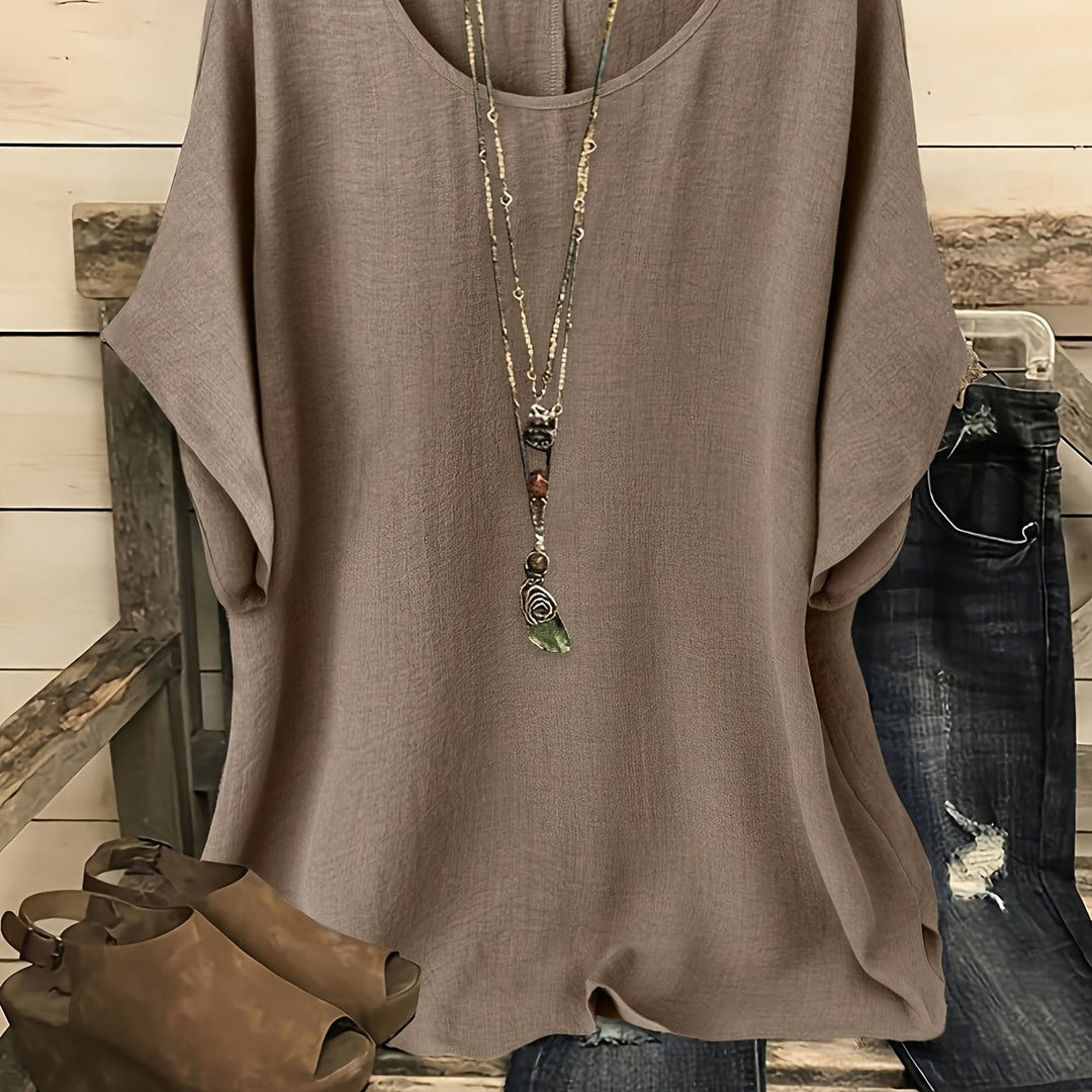 Taupe loose summer top on hanger with necklace, sandals, and jeans on rustic bench.