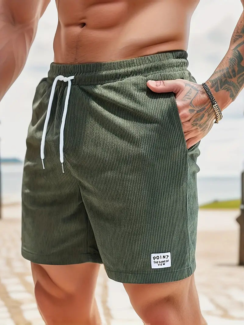 Close-up of green swimming trunks with drawstring, worn by model on a sunny beach.