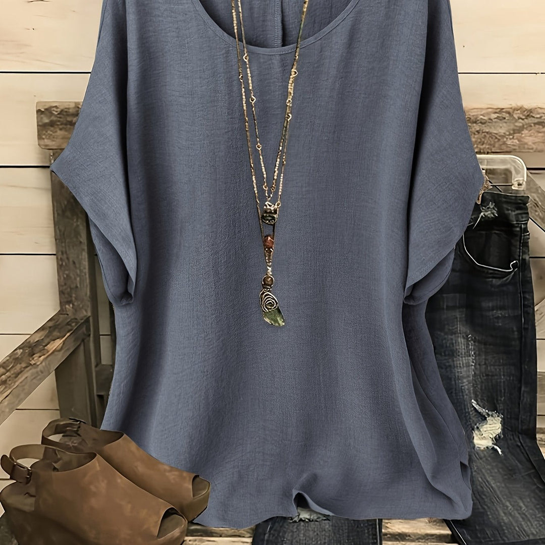 Slate gray loose summer top on hanger with necklace, sandals, and jeans on rustic bench.