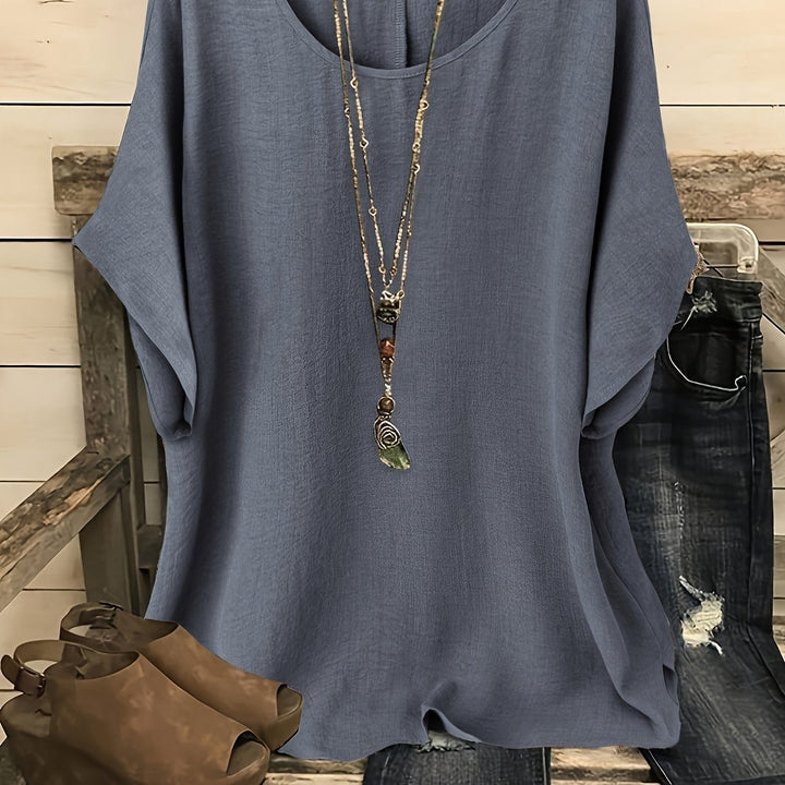 Slate gray loose summer top on hanger with necklace, sandals, and jeans on rustic bench.