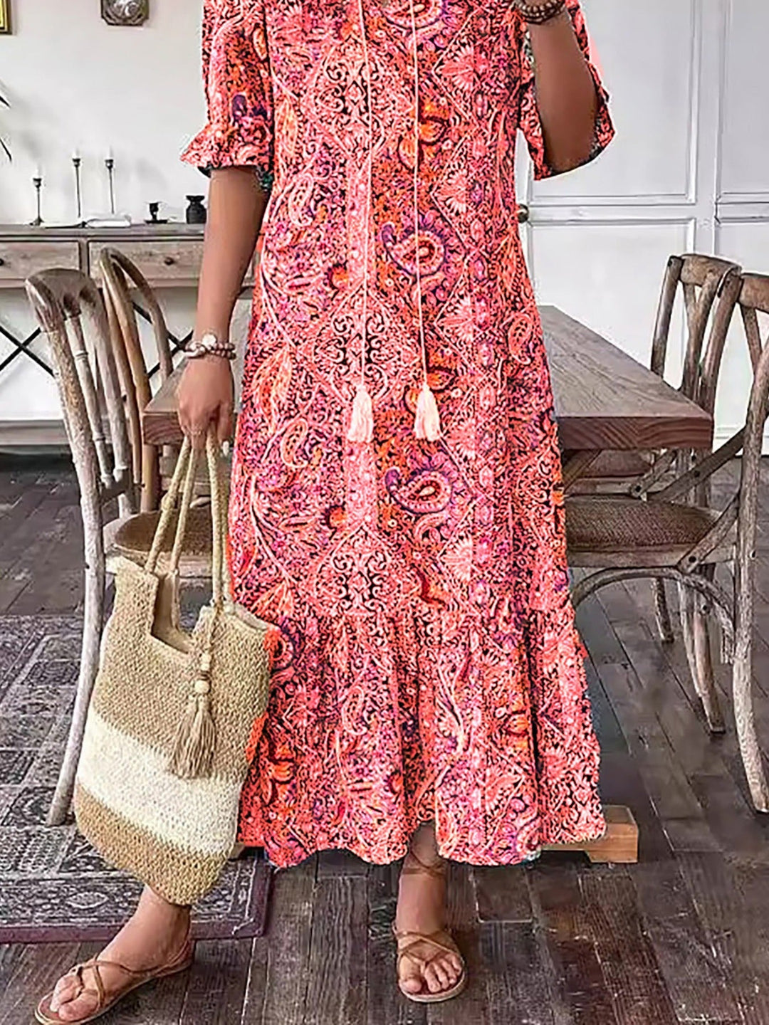 Close-up of vibrant pink boho dress, woman holding straw bag, indoor setting with rustic wooden flooring and décor.