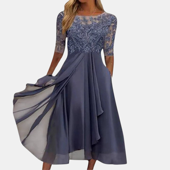 Elegant dark blue dress with lace bodice and flowing skirt, studio background.