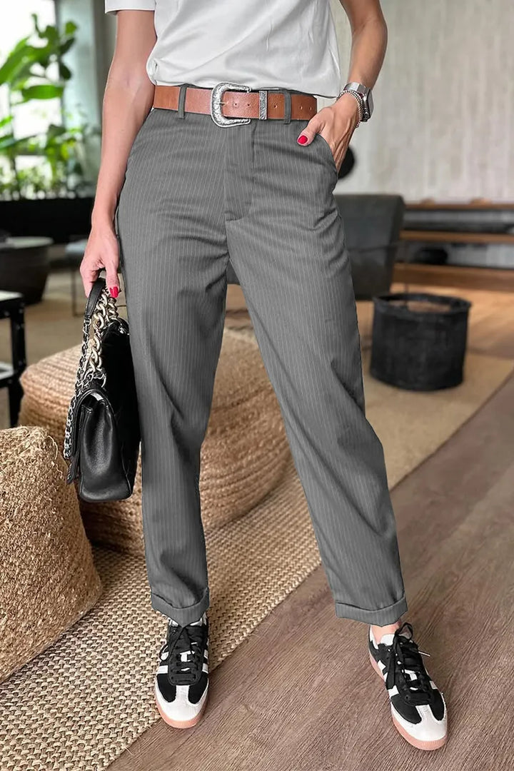 Gray pinstripe pants in a bright indoor space, styled with a brown belt and accessorized with a handbag.