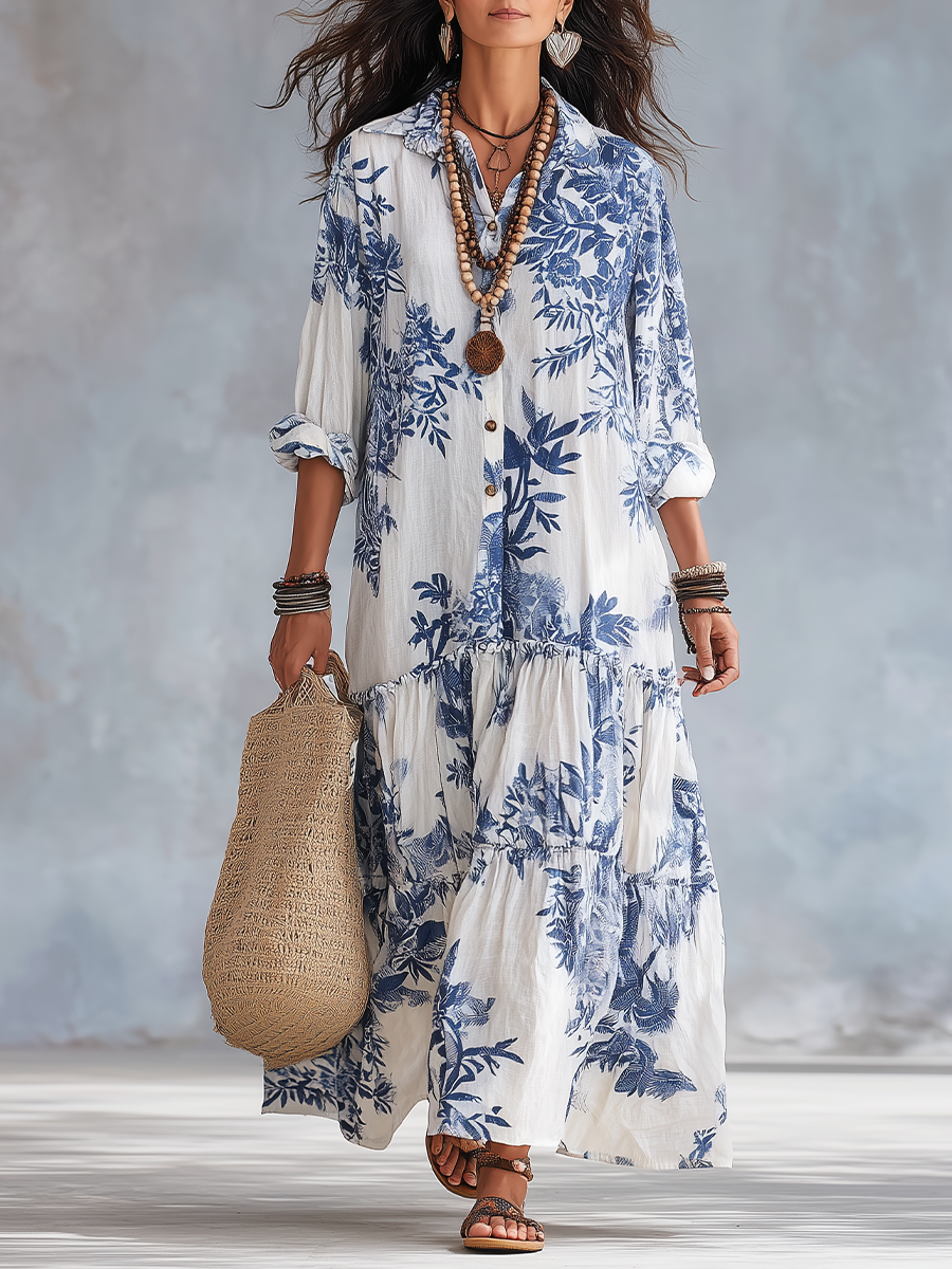 Flowing white maxi dress with blue floral print, worn with layered necklaces and bracelets, holding woven bag in soft studio light.