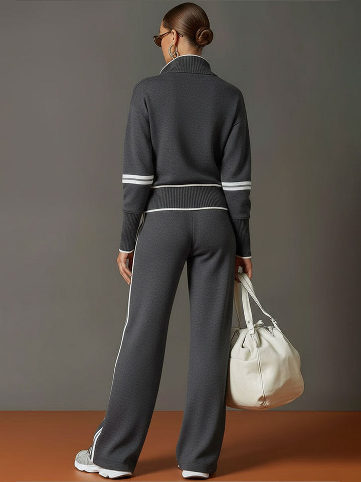 Back view of matching lounge set in dark gray with contrast stripes, paired with white sneakers and a bag in a studio setting.